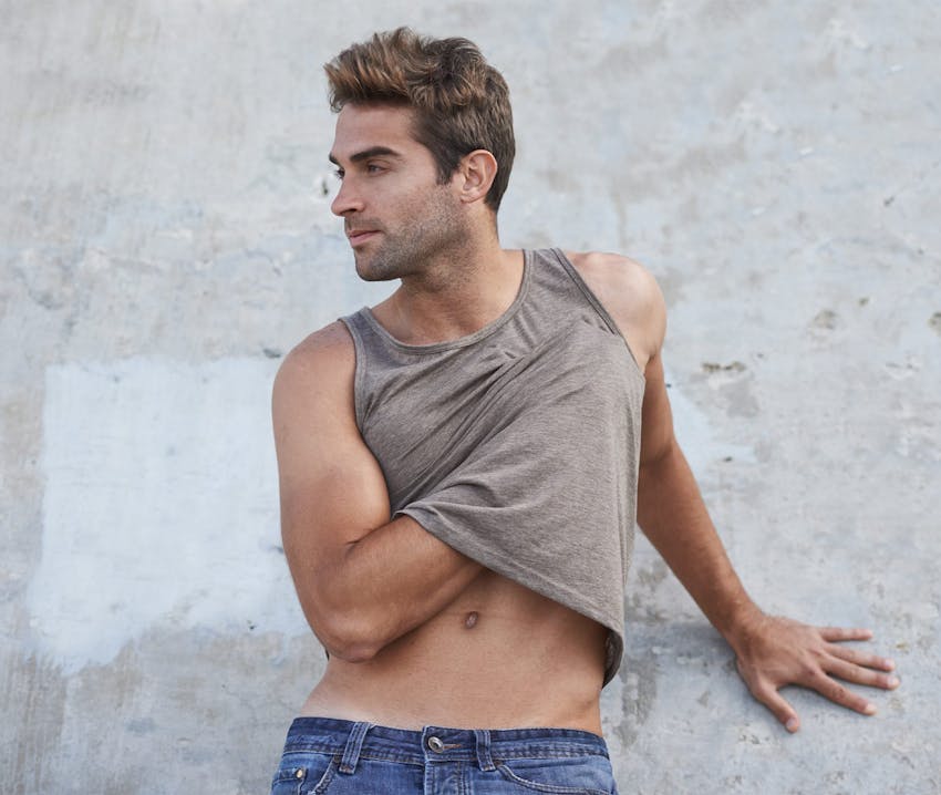 man with hand under his tank up touching his chest looking to the left