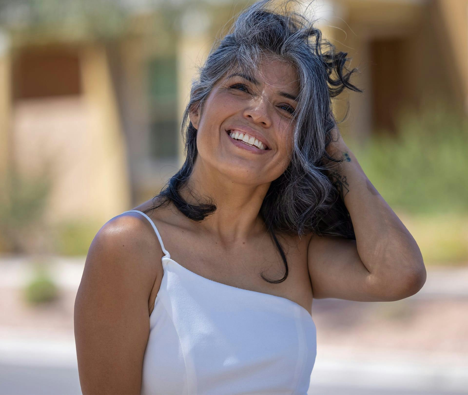 older woman in white shirt holding hair back and smiling
