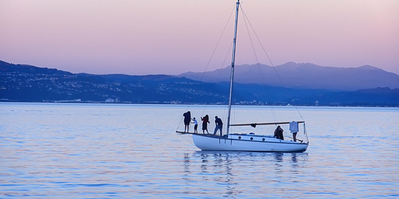 People enjoy the sunset on a sailboat in the ocean harbour in Wellington, New Zealand