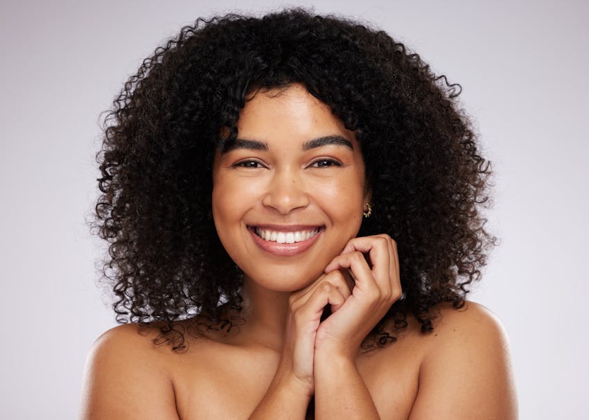 model with curly hair smiling and holding hands together