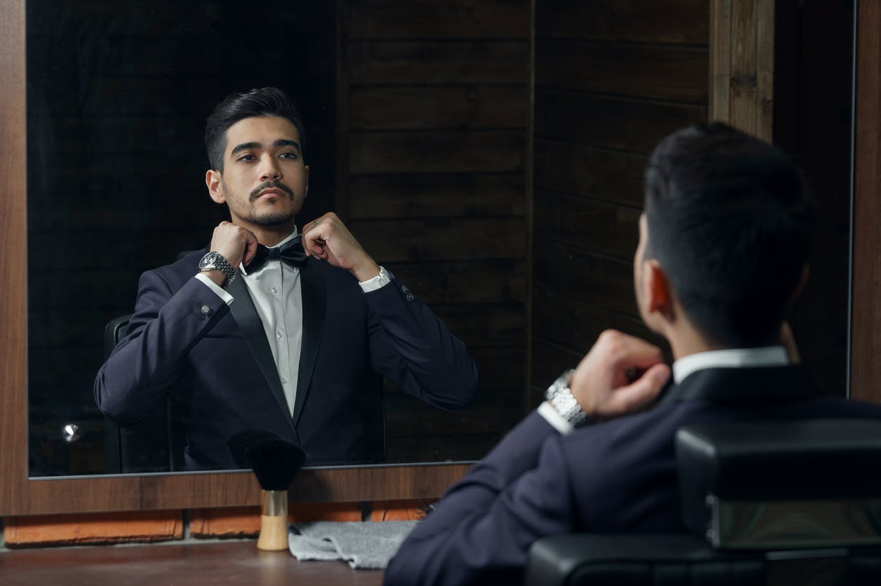 male model in tuxedo looking into mirror
