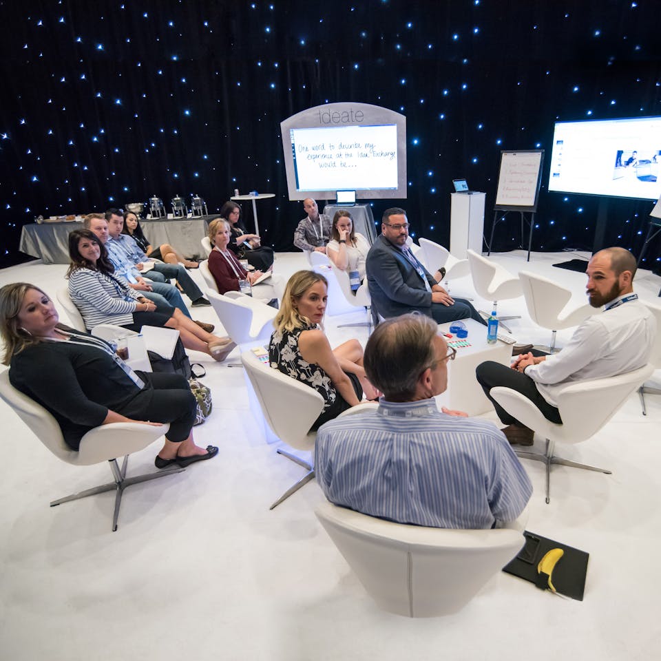 A group of men and women sitting white comfy chairs with a black background with fake stars.