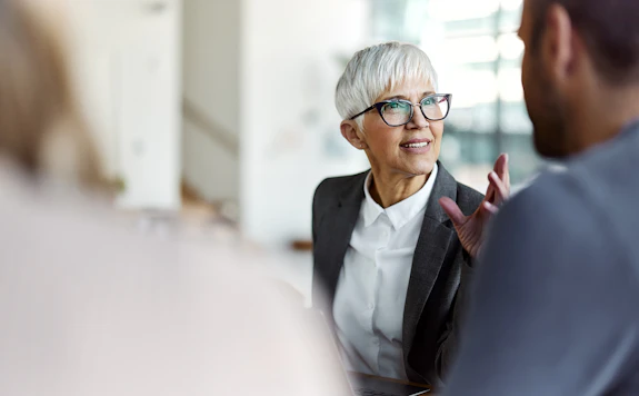 A woman wearing glasses speaks to a man