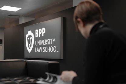 A woman reading a document infront of a BPP University Law School sign