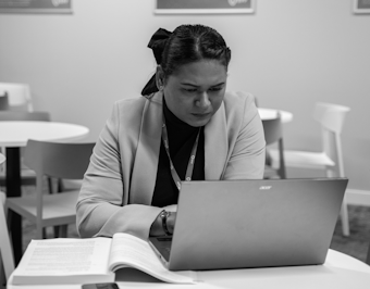 A female student works on a laptop alongside an opened book