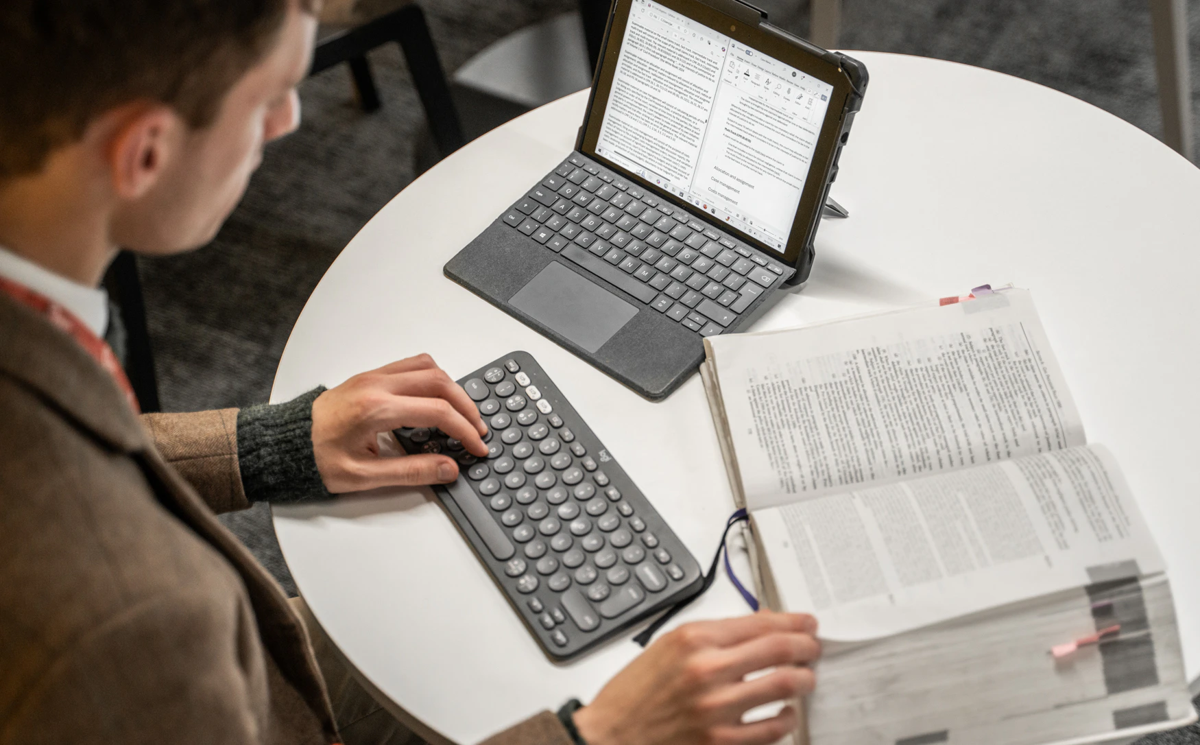 A law student is typing on a keyboard, next to a tablet computer and open law book