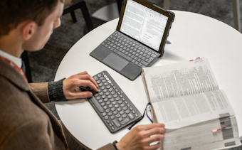 A law student is typing on a keyboard, next to a tablet computer and open law book