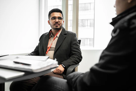 A male sits in a meeting room talking to another person A male sits in a meeting room talking to another person