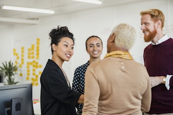 A group of men and woman have a standing conversation in an office
