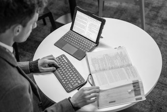 A man sits at a desk with a large law textbook and a tablet computer