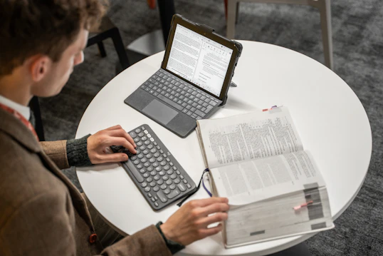 A student reads a large law textbook sitting on a desk next to a tablet computer
