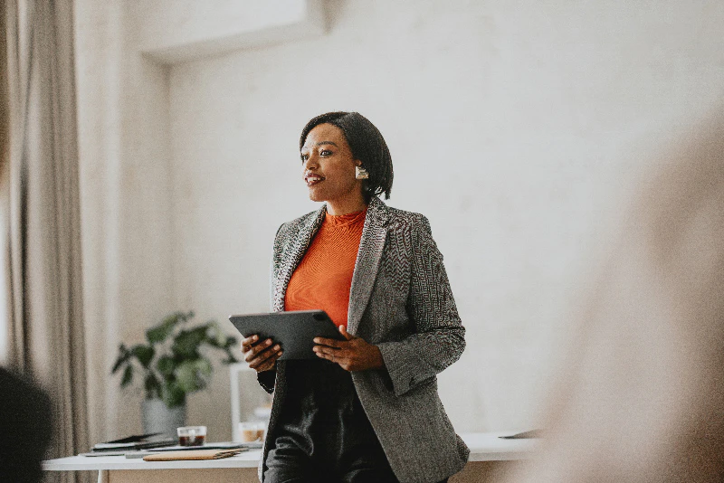 A woman stands as she presents while holding a tablet computer