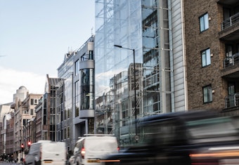 A busy London street with numerous modern buildings and vehicles driving by