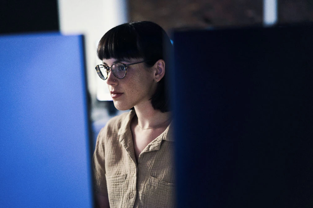 A woman wearing glasses works on a blue desktop computer