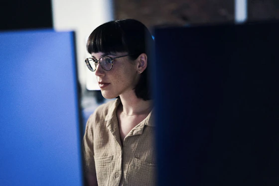 A woman wearing glasses works on a blue desktop computer