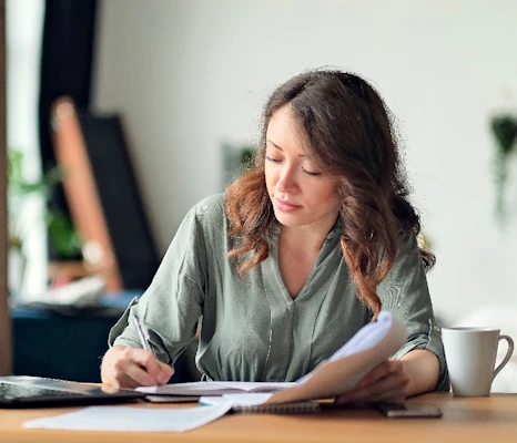 A woman writes on a notepad whilst sitting at a desk with a coffee mug