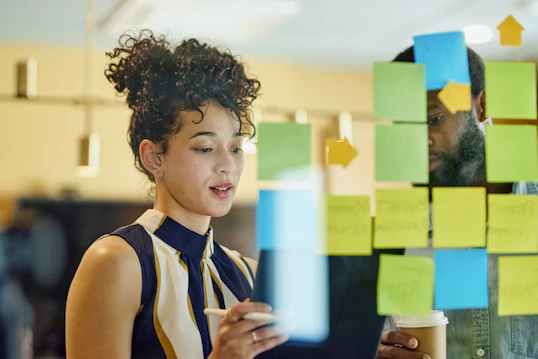 A man and woman stand at a large glass window filled with different coloured post it notes