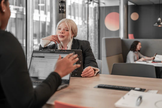 Two students with laptops sit across a desk