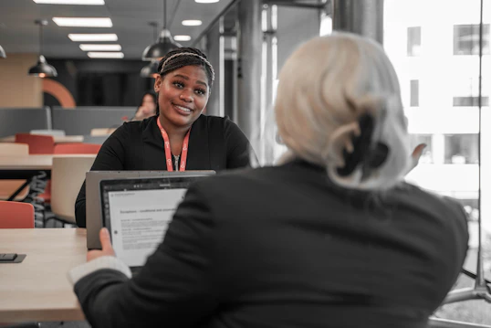 Two students with laptops sit across a desk