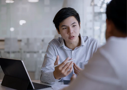 A man with a tablet computer speaks to a colleague over a desk