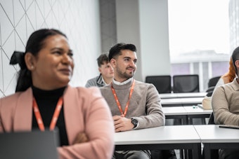 Students sit in a class at a row of tables