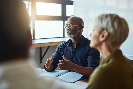 People having a meeting at a boardroom table with someone gesturing.