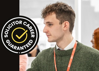 A woman with glasses sits in a BPP centre booth with a laptop. There is a Solicitor Career Guaranteed badge