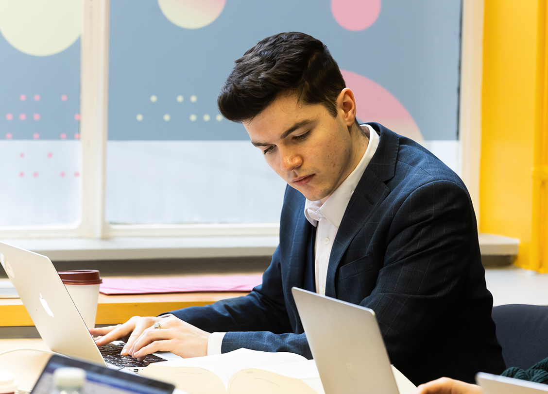A man in a suit works from a desk at a BPP centre. Solicitor Career Guaranteed badge is shown.