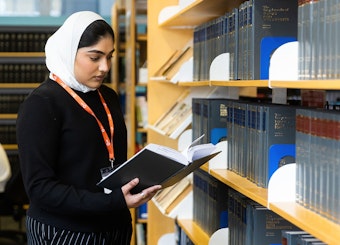 A female student wearing a lanyard reads a law book in a library