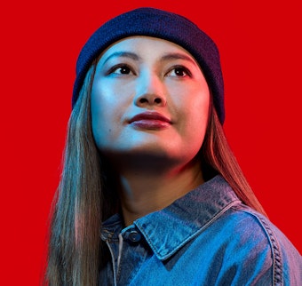 A woman in a blue denim shirt and blue beanie hat looks into the distance