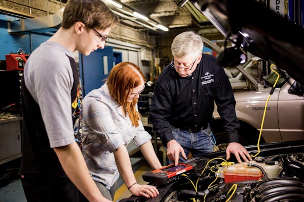 Two students works on a car in a garage with a teacher