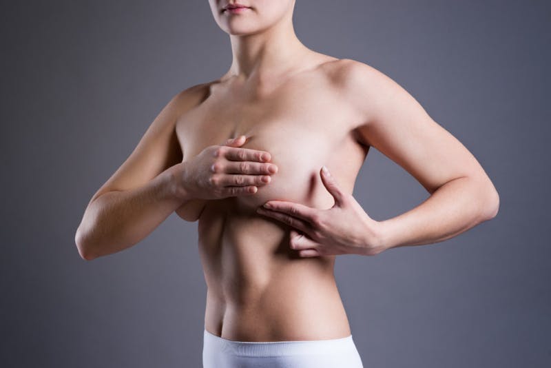 close up of a woman displaying her left breast while covering her breast with her hands