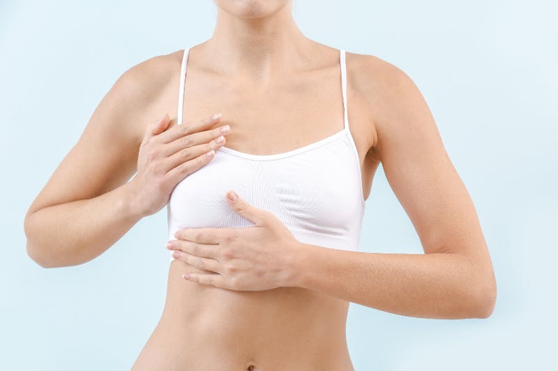 close up of a woman's chest in a white bra covering holding her right breast with both hands