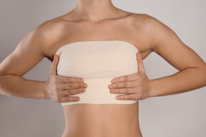 woman in a tan chest wrap with her hands holding her breasts