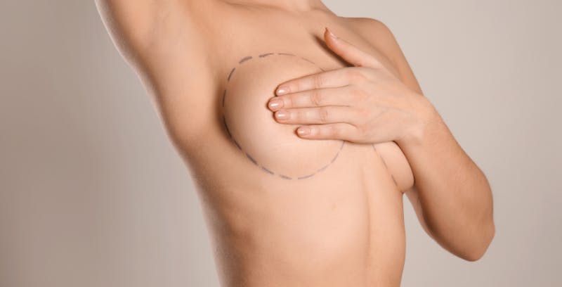 close up of a woman's chest in the nude and her hands covering her breasts
