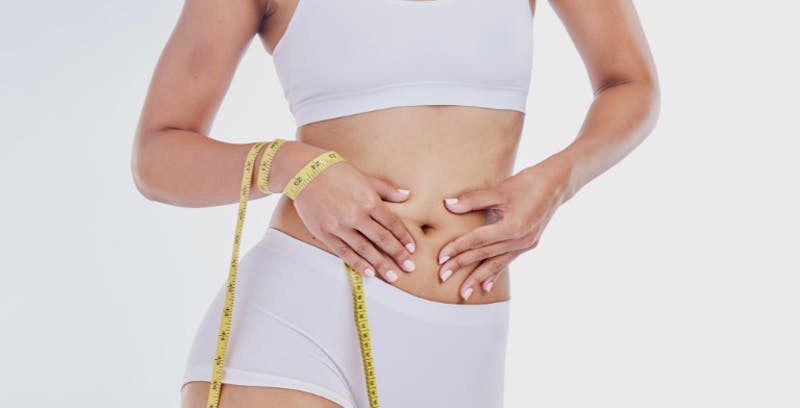 woman in white underwear and bra has a measuring tape around her wrist while her hands are on her stomach