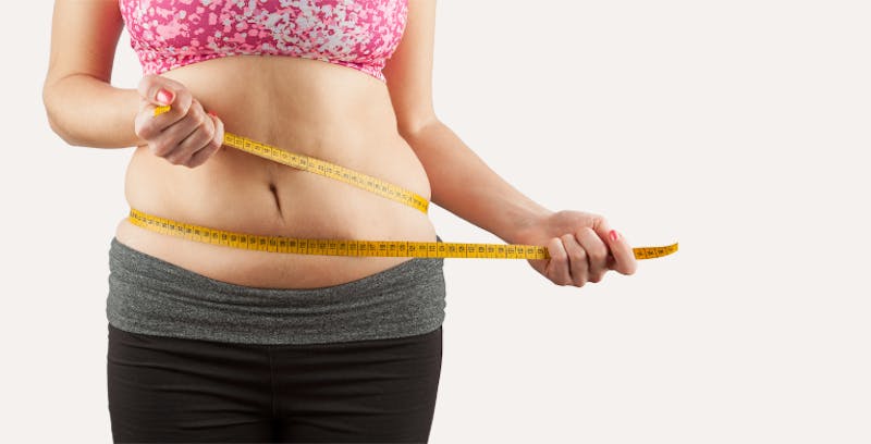 close up of a woman in a pink top holding a measuring tape around their waist