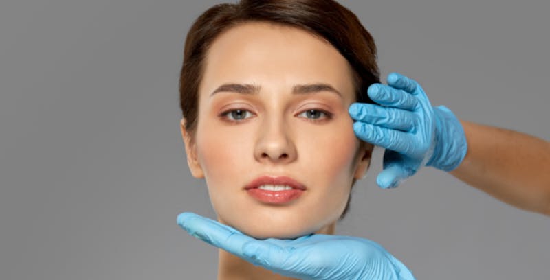 woman with someone in blue surgical gloves examining her face