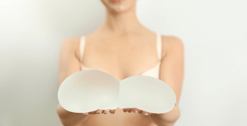 woman in a bra holding up breast implants
