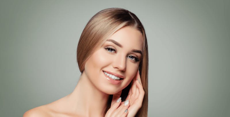 blond woman with long straight hair smiling and touching her face