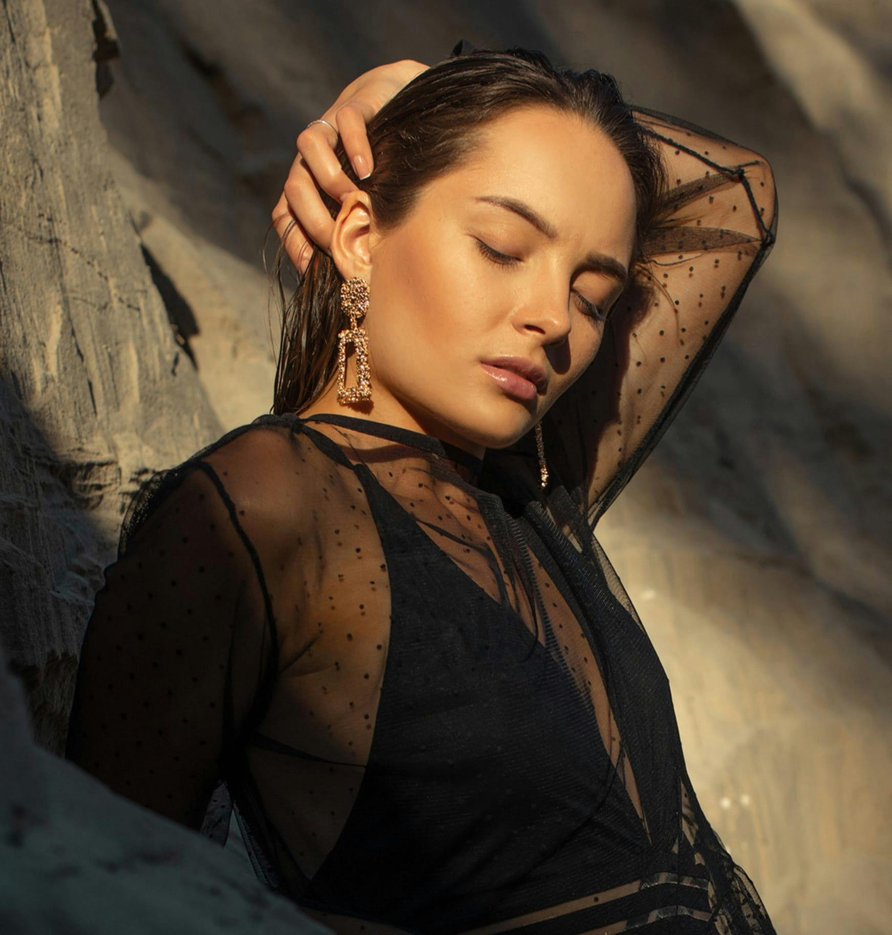 woman in a see through black dress and black top leaning against a rock posing for picture