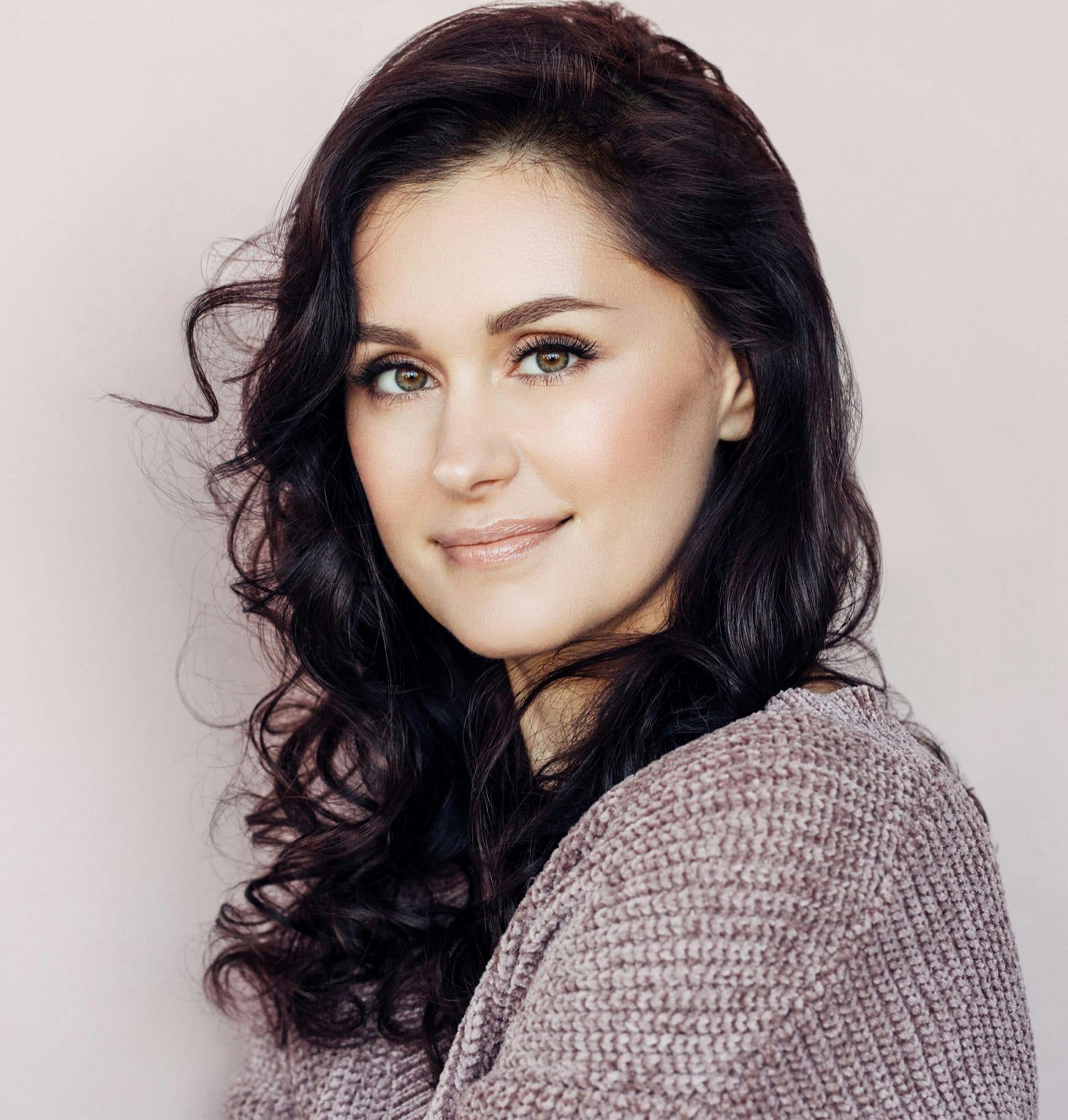 woman with long dark hair and a sweater on smiling at camera
