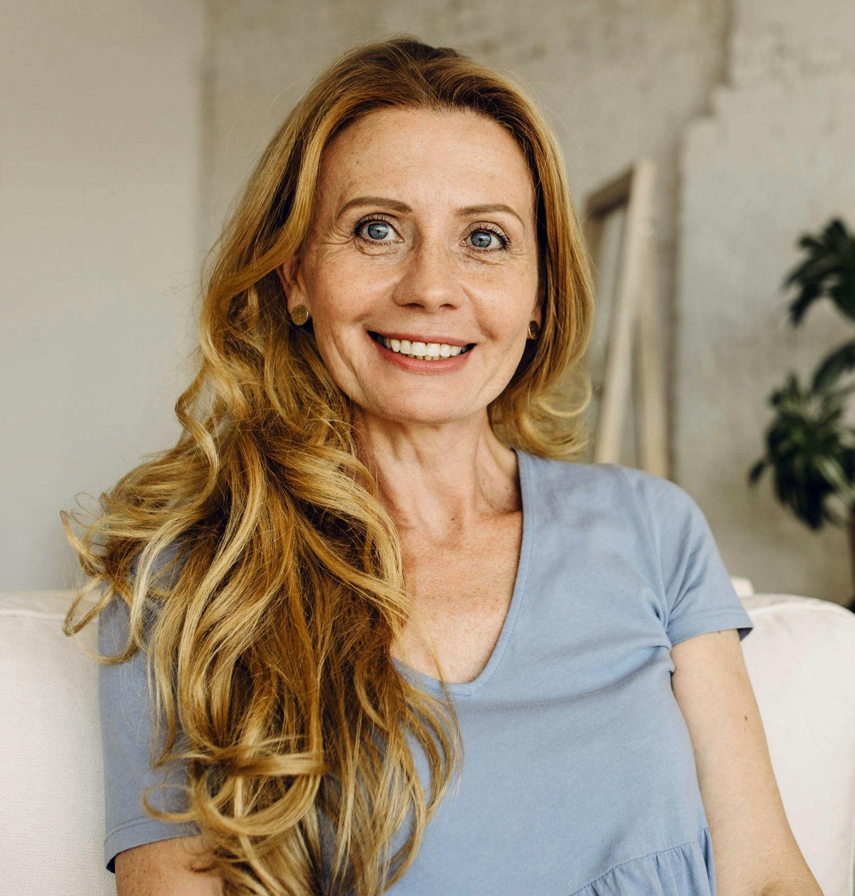 blond woman with long wavy hair sitting on a white couch