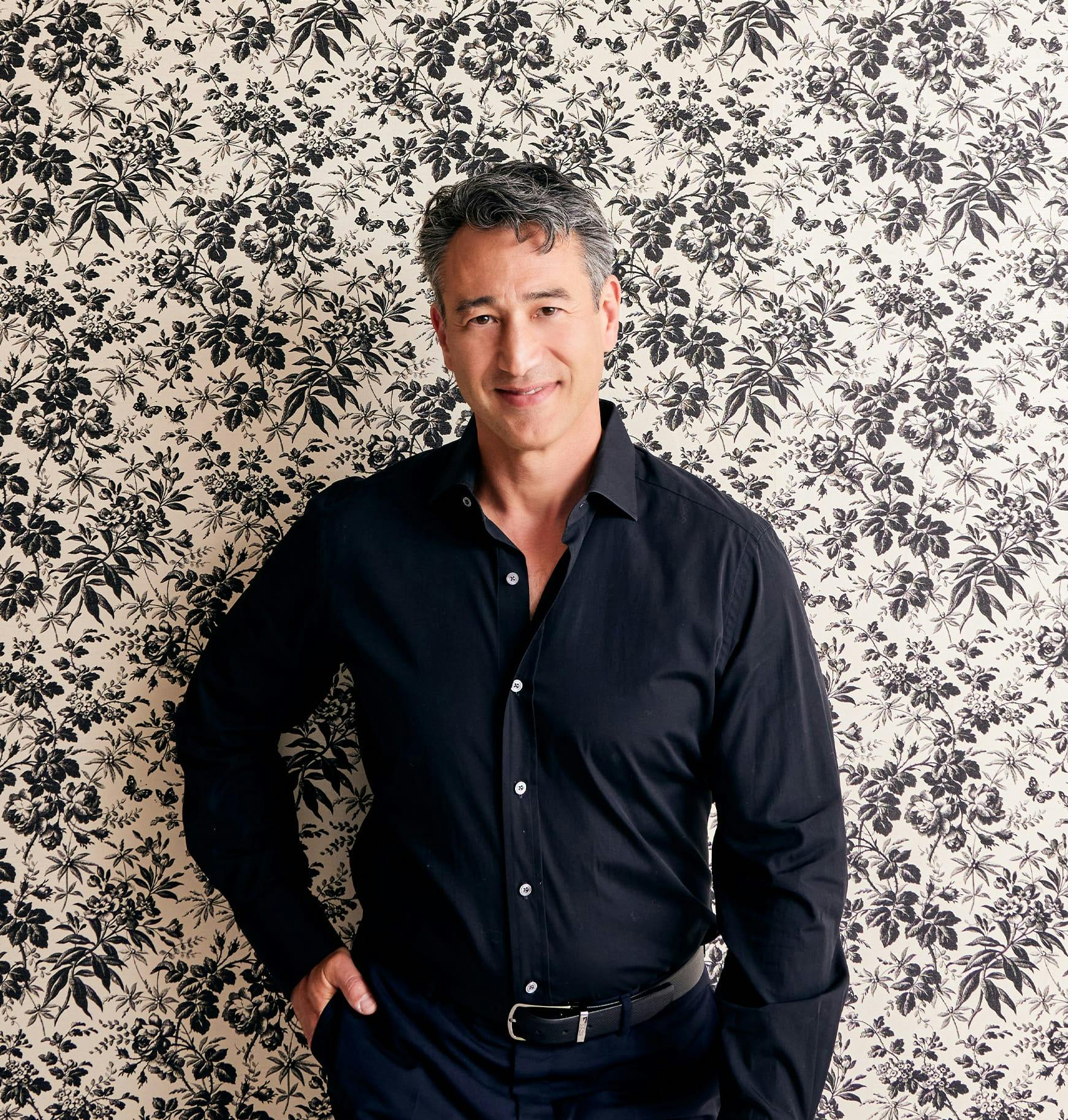 Dr. Leif Rogers in a black shirt and blue pants standing in front of a wall