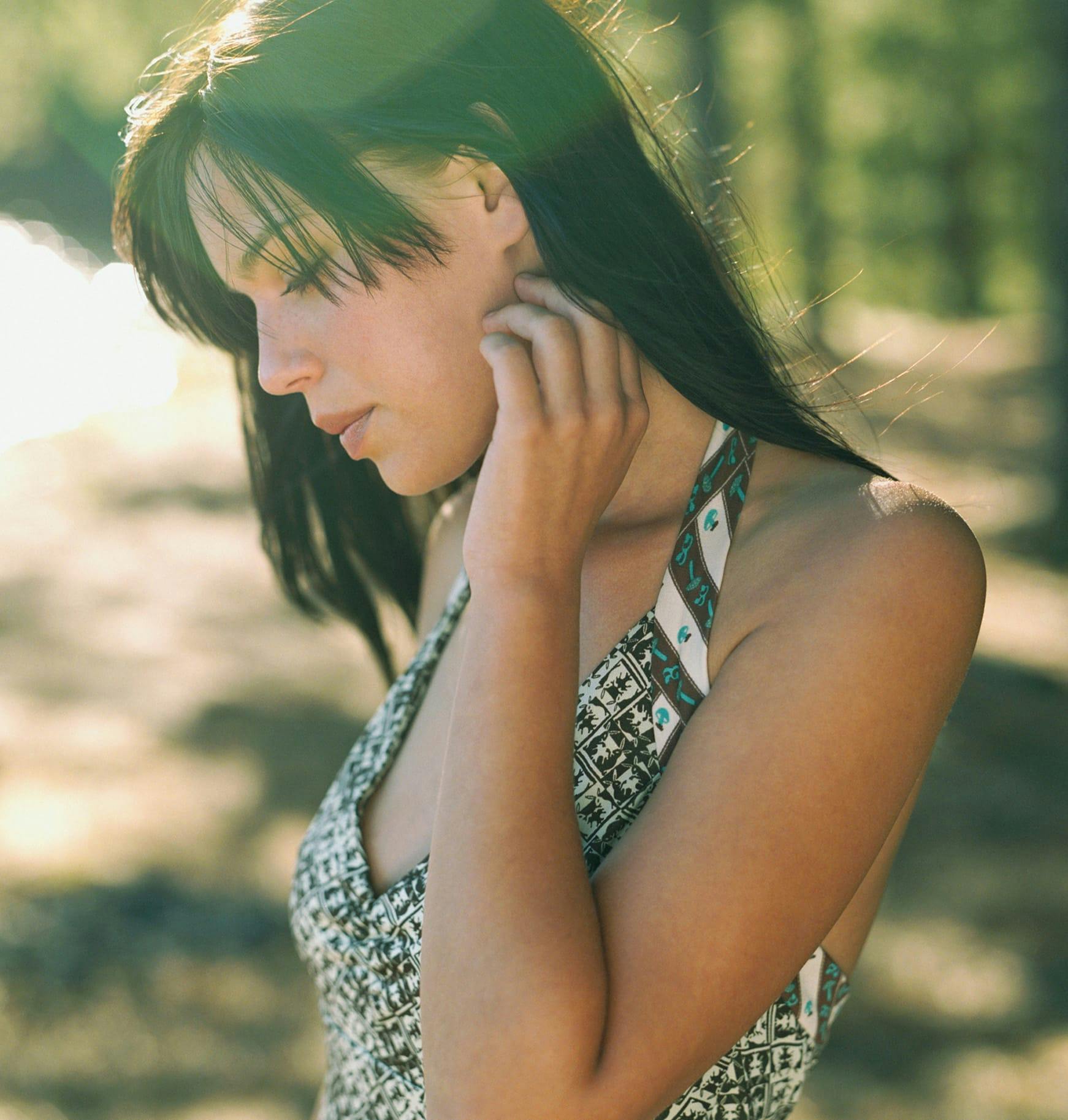a woman in patterned top posing on beach with hand to face