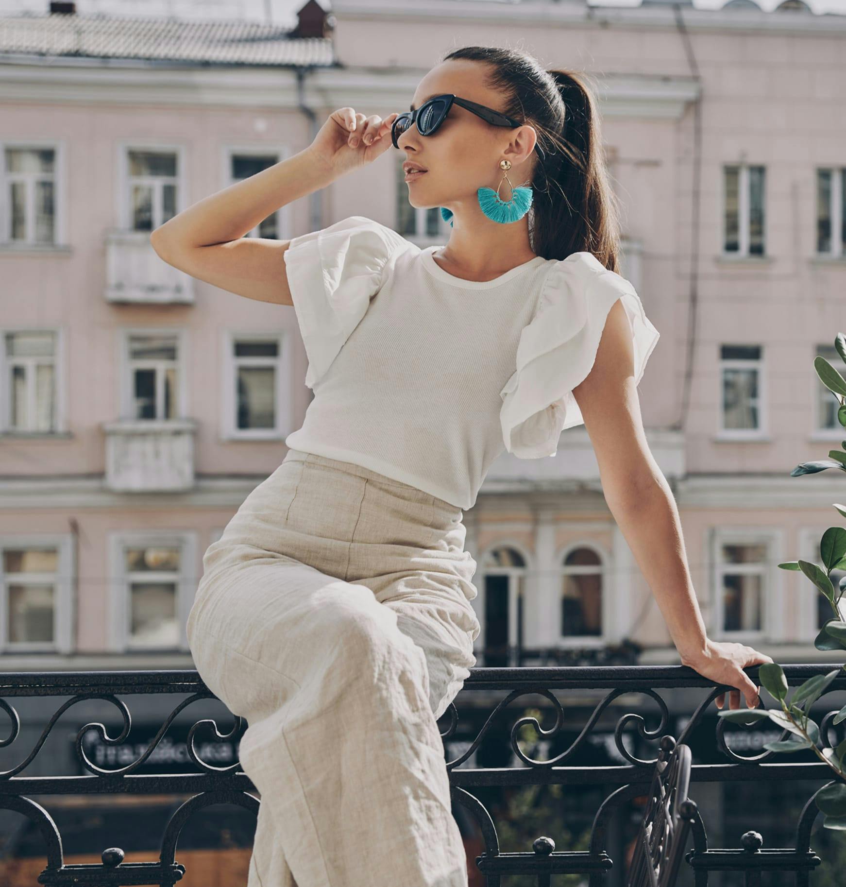 woman in white top and white pants sitting on a railing