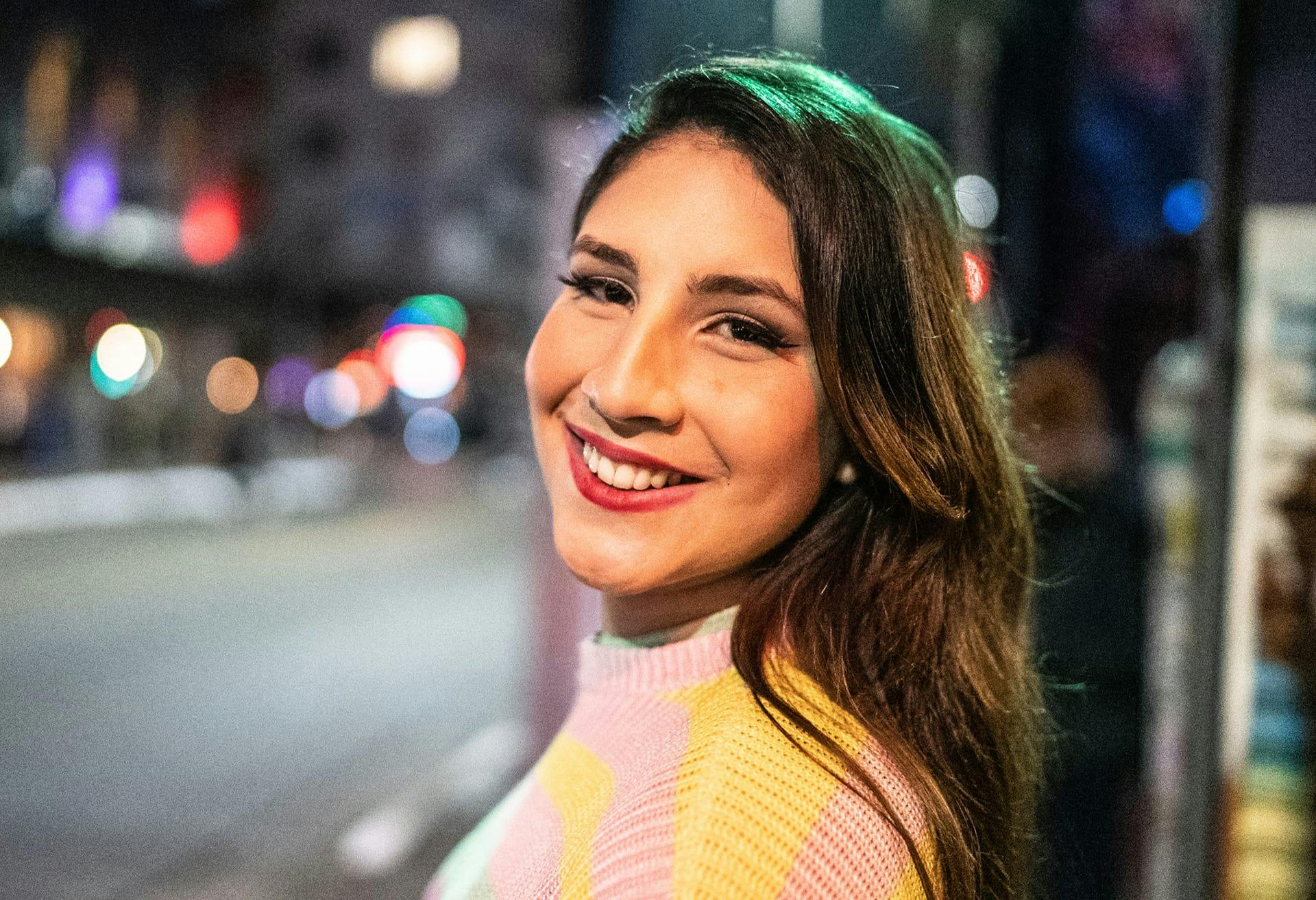 Woman with long brown hair wearing a pink and yellow sweater