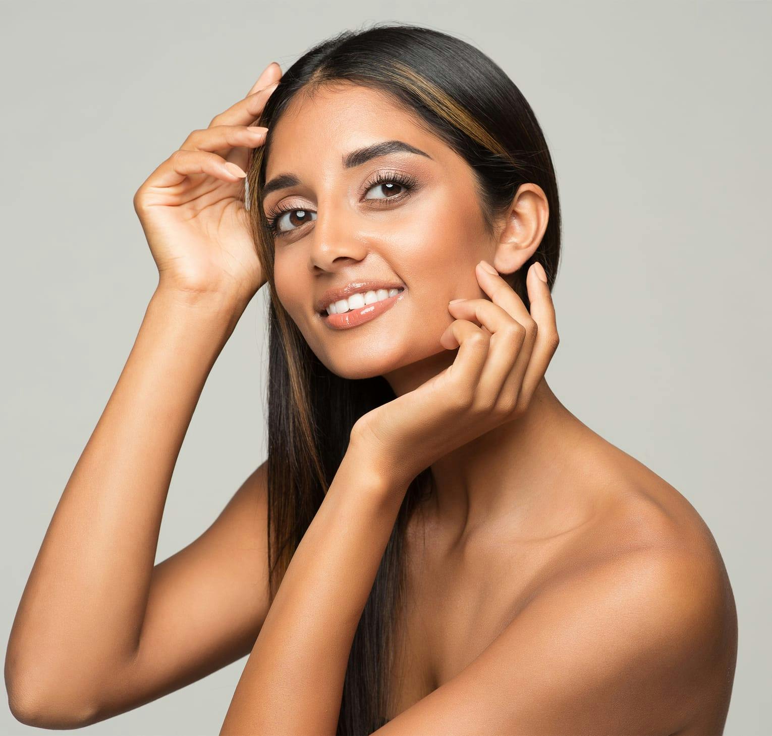 woman with long brown hair touching her face