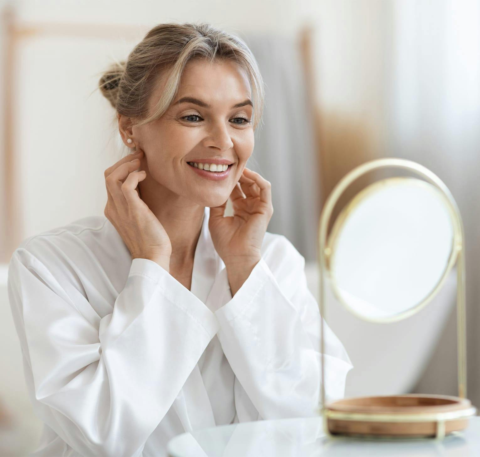 woman in robe looking at her face in a mirror