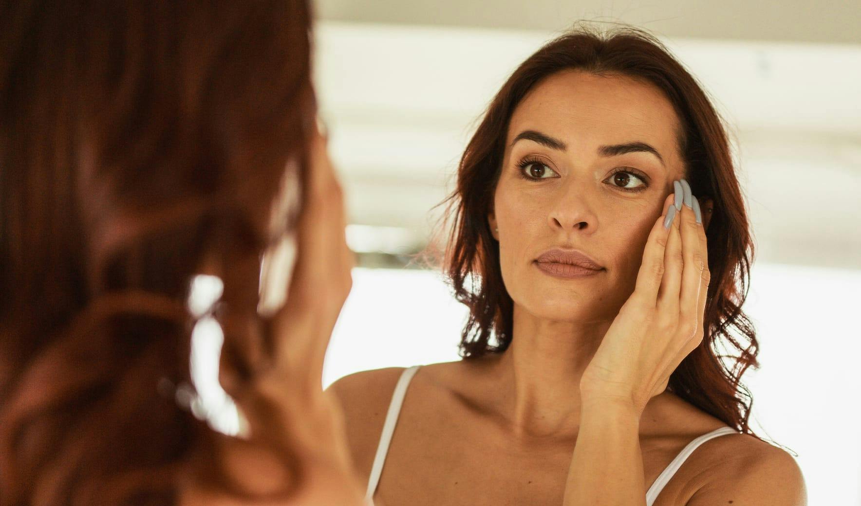woman looking in mirror touching her face